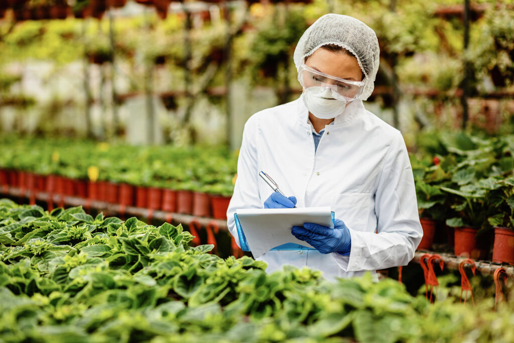Female scientist writing notes while examining plants in a greenhouse.